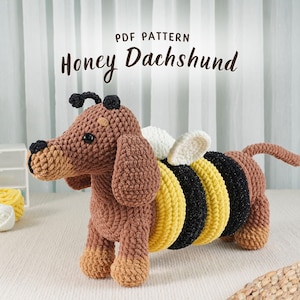 Puede incluir: Un perro salchicha de ganchillo con detalles de abeja. El perro es marrón con un hocico y patas color canela, y tiene un cuerpo a rayas negro y amarillo con alas blancas. El texto "PDF PATTERN Honey Dachshund" está en la parte superior.