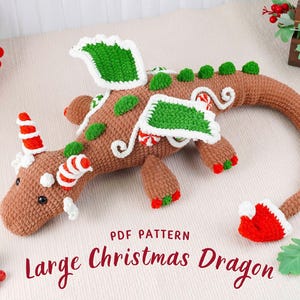 Puede incluir: Un dragón de ganchillo marrón con detalles verdes y blancos, diseñado para Navidad. El dragón presenta detalles de bastones de caramelo rojos y blancos, alas verdes y un gorro de Papá Noel rojo en la cola. El texto "Large Christmas Dragon" es visible.