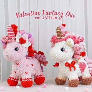 May include: Two crocheted unicorn plushies. One is pink with red accents and heart details, the other is white with pink accents. Both have curly manes, horns, and are decorated with bows. The text "Valentine Fantasy Duo PDF Pattern" is at the top.