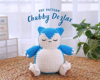 May include: PDF pattern for a crocheted blue and white Snorlax plush toy. The toy is sitting on a woven straw mat.