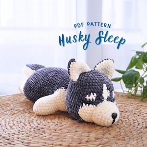 Könnte beinhalten: PDF-Muster zum Häkeln eines schlafenden Huskys. Der Husky ist grau und weiß und liegt auf einer gewebten Matte. Der Text "PDF PATTERN Husky Sleep" befindet sich oben im Bild.