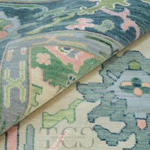 May include: A hand-knotted area rug featuring a folded corner that reveals a cream-coloured base with intricate floral and geometric patterns in shades of teal, sage green, and soft pink. The text THE CARPET SAGA is visible in the centre.