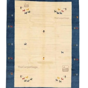 May include: Rectangular rug with a cream-colored center and a dark blue border. The rug features small, colorful figures and the text "TheCarpetSaga". The rug has a traditional design.