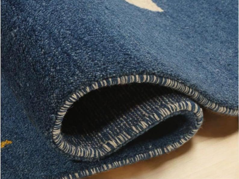 May include: Close-up of a rolled-up blue rug with a white and yellow pattern. The rug has a textured surface and a white stitched border. The rolled section reveals the underside of the rug.