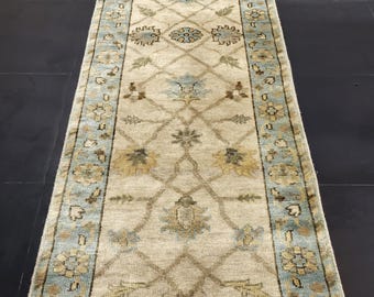 May include: A beige runner rug with a blue and brown floral pattern. The rug has a fringed edge.