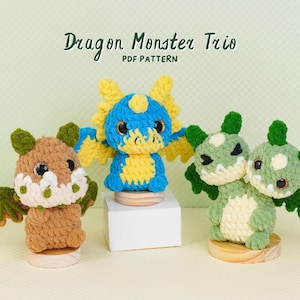May include: Three crocheted dragon monster figures with black eyes and textured yarn. The text Dragon Monster Trio PDF PATTERN is displayed above. The figures are brown, blue and yellow, and light green, each standing on a small wooden base.