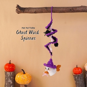 May include: A crochet wind spinner featuring a spiral design in purple, black, and white, hanging from a wooden branch. At the bottom, a small white ghost wears a purple witch hat. Text reads: PDF PATTERN Ghost Wind Spinner.