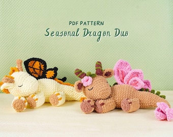 Könnte beinhalten: Zwei gehäkelte Drachen-Plüschtiere in Creme und Braun, mit orangefarbenen, schwarzen und rosa Akzenten. Der cremefarbene Drache hat Schmetterlingsflügel, während der braune Drache Blumendetails hat. Der Text "PDF PATTERN Seasonal Dragon Duo" steht oben.
