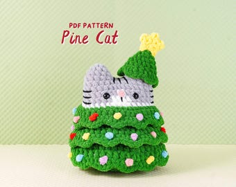 May include: A crocheted cat figure wearing a green Christmas tree costume with colorful pom-poms. The cat has gray and white fur with black stripes and a yellow star on top. Text on the image reads "PDF PATTERN Pine Cat."