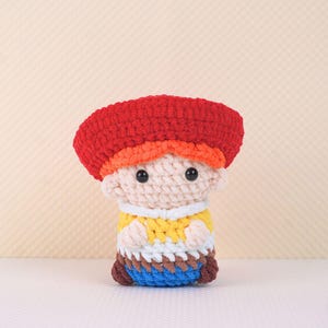May include: A crocheted toy figure of a person wearing a red hat, orange hair, a yellow shirt, white pants, and blue shoes.