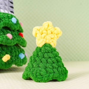 Peut inclure: Petit sapin de No&euml;l crochet&eacute; &agrave; la main, surmont&eacute; d'une &eacute;toile jaune. L'arbre est vert avec une surface textur&eacute;e et l'&eacute;toile est jaune vif. Une d&eacute;coration festive.