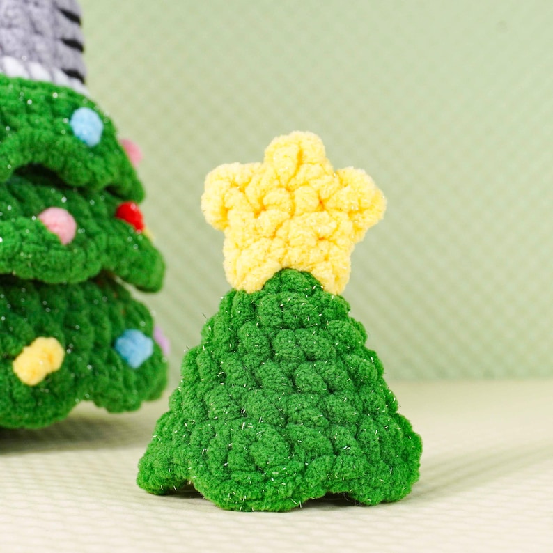 Peut inclure: Petit sapin de No&euml;l crochet&eacute; &agrave; la main, surmont&eacute; d'une &eacute;toile jaune. L'arbre est vert avec une surface textur&eacute;e et l'&eacute;toile est jaune vif. Une d&eacute;coration festive.