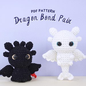 May include: PDF pattern for crocheting a pair of dragons. One dragon is black with red accents and the other is white. Both dragons have large eyes and are posed with their wings spread.