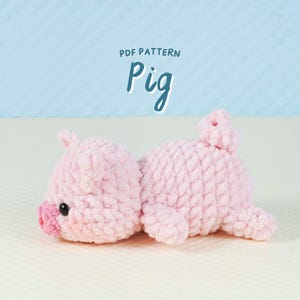 Puede incluir: Un juguete de cerdito rosa hecho a mano con ganchillo. El cerdito está tumbado, con un hocico rosa, ojos negros pequeños y una cola rizada. El texto "PDF PATTERN" y "Pig" están en el fondo.