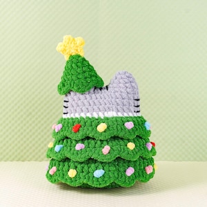 Peut inclure: Un sapin de No&euml;l en forme de chat crochet&eacute;. Le sapin est vert avec des pompons color&eacute;s et une &eacute;toile jaune au sommet. La t&ecirc;te du chat est grise avec des rayures noires. D&eacute;coration de vacances faite &agrave; la main.