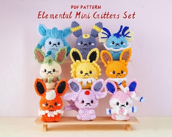 May include: A collection of nine colorful, crocheted creatures with large ears and expressive faces, displayed on a small wooden shelf. The text "PDF PATTERN Elemental Mini Critters Set" is at the top. Each critter has unique color combinations.