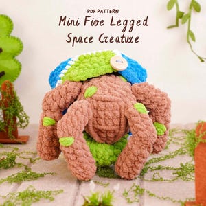 May include: A crochet plush toy shaped like a five-legged space creature in brown, lime green, and blue yarn. The creature features a small wooden button on its blue cap. The text above the creature reads: PDF PATTERN Mini Five Legged Space Creature.