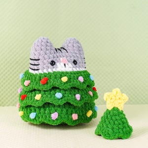 Peut inclure: Un sapin de No&euml;l en crochet fait main en forme de chat, avec une t&ecirc;te de chat grise et un corps de sapin vert orn&eacute; de d&eacute;corations color&eacute;es. Un petit sapin vert avec une &eacute;toile jaune est &agrave; c&ocirc;t&eacute;. Une d&eacute;coration de vacances unique.