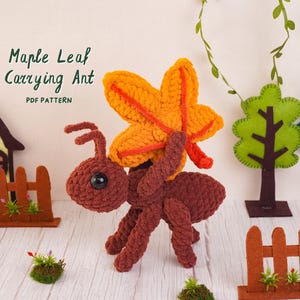 Pode incluir: Um brinquedo de formiga em crochê marrom carregando uma grande folha de bordo laranja e amarela nas costas. O texto Maple Leaf Carrying Ant PDF PATTERN é visível no canto superior esquerdo. A formiga tem cabeça redonda, olhos pretos e seis pernas.