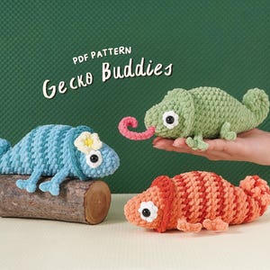 May include: Three crocheted gecko toys in shades of blue, green, and orange. The blue gecko rests on a wooden log, while the green gecko has a pink tongue extended. The orange gecko is on a white surface. Text reads "PDF Pattern Gecko Buddies."
