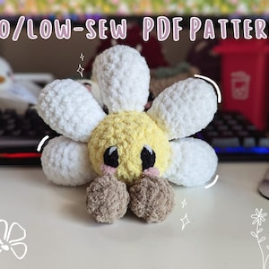 Puede incluir: Una flor de margarita de crochet con un centro amarillo y pétalos blancos. La flor tiene dos pompones marrones para los ojos y una nariz rosa. La flor está sentada sobre una superficie blanca. NO/LOW-SEW PDF PATTERN.