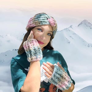 May include: A matching crochet headband and fingerless gloves set. The set features a blend of pastel colors, including pink, blue, and beige. The items are designed with a textured stitch, perfect for cold weather. The background shows a snowy mountain range.
