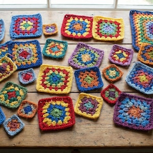 May include: A collection of colorful, handmade crochet squares in various sizes and vibrant hues. The squares feature intricate patterns with a central design, surrounded by multiple rounds of contrasting colors. The arrangement is on a wooden surface.