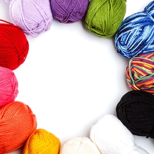 May include: A collection of colorful yarn balls arranged in a semi-circle on a white background. The yarn colors include red, pink, orange, yellow, white, black, blue, green, purple, and a multi-colored skein. Ideal for knitting and crochet projects.