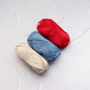 May include: Three skeins of yarn in red, blue, and beige are arranged diagonally on a textured white surface. The yarn is tightly wound, suggesting it's ready for knitting or crocheting projects. The colors offer a versatile palette for various crafts.