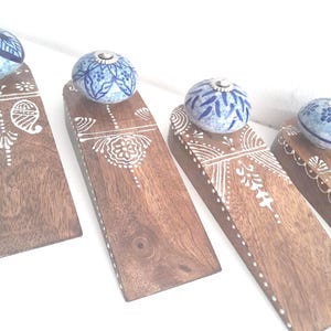 May include: Four wooden doorstops with blue and white ceramic knobs. Each doorstop has a different white painted design.