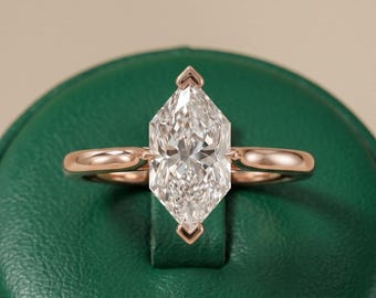 Op de afbeelding: Een roségouden ring met een grote, marquise-geslepen diamant. De diamant is gezet met delicate pootjes aan de boven- en onderkant, en de band heeft een glad, afgerond ontwerp. De ring wordt getoond op een groene ondergrond.