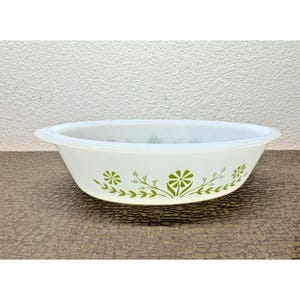May include: White oval serving dish with a green floral pattern. The dish has a simple design with a slightly flared rim and a series of green flowers and leaves around the exterior. The dish is likely made of glass.