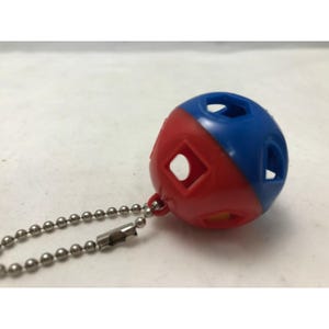 May include: A small, two-toned ball keychain. The top half is blue, and the bottom half is red. The ball has several geometric cutouts and is attached to a silver ball chain.