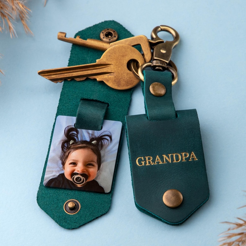 May include: A green leather keychain with a photo of a baby and the word "GRANDPA" in gold lettering. The keychain has a brass key ring and two keys.