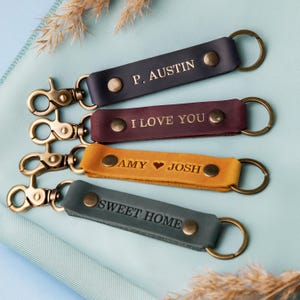 May include: Four leather keychains with gold metal rings and clasps. The keychains are personalized with the text "P. Austin", "I Love You", "Amy ♥ Josh", and "Sweet Home".