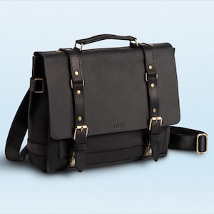 May include: Black leather messenger bag with a top handle, shoulder strap, and buckle closures. The bag features gold-colored hardware and the initials "PEV" embossed on the front. The bag is designed for carrying items.