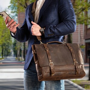 May include: A brown leather messenger bag with a flap closure, two buckle straps, and a shoulder strap. The bag has a handle on top and gold-colored hardware. The bag is worn over the shoulder.