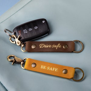 May include: Two leather keychains with metal rings and clasps. The brown keychain has the text "Drive safe" in gold lettering. The yellow keychain has the text "BE SAFE" in gold lettering.