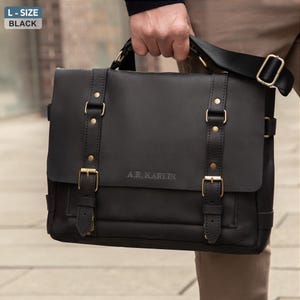 May include: Black leather messenger bag with a flap closure, adjustable shoulder strap, and gold-colored metal hardware. The bag has two front straps with buckles and the text "A.R. Karlin" embossed on the front.
