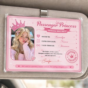 May include: A rectangular pink Passenger Princess official document card in a clear plastic holder. It features a photo of a person with blonde hair, a crown graphic, and text including Issued to: Carolyn, Expiration Date: Never, and Valid Through: Forever.