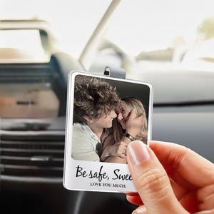 May include: A clear, rectangular car charm with a photo of a couple. The charm has a silver clip for hanging and the text "Be safe, Sweet" and "LOVE YOU MUCH." is printed on the bottom.