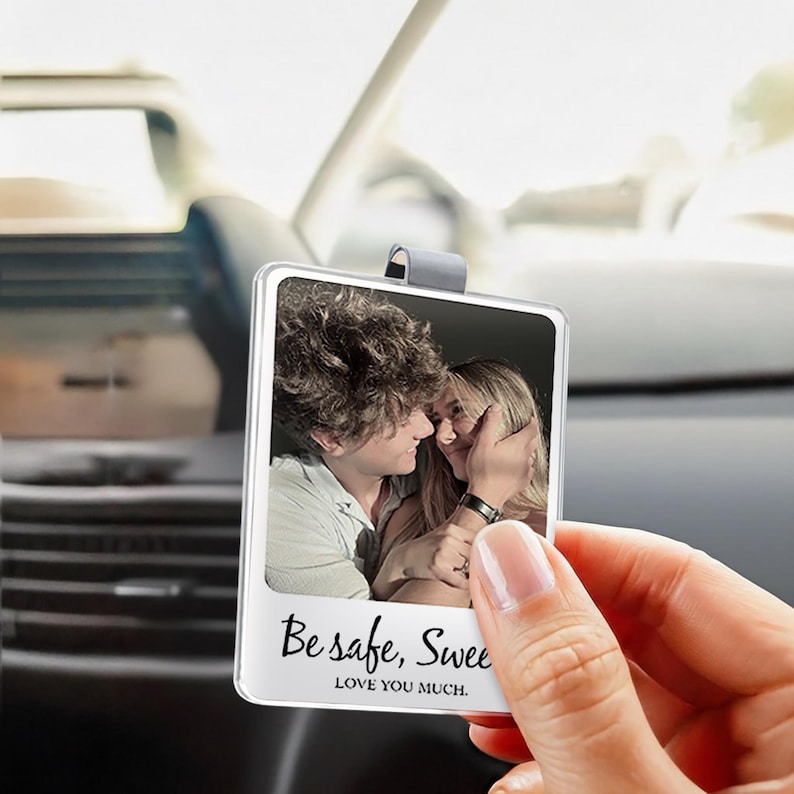 May include: A clear, rectangular car charm with a photo of a couple. The charm has a silver clip for hanging and the text "Be safe, Sweet" and "LOVE YOU MUCH." is printed on the bottom.