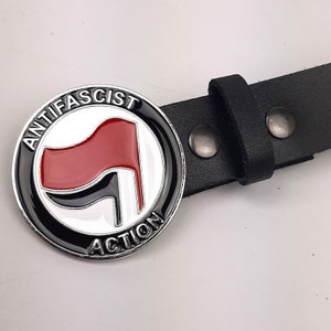 May include: A black leather belt with a silver buckle featuring a red and black anti-fascist symbol with the text "Anti-Fascist Action".