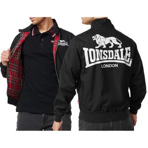 Può includere: Giacca nera con fodera a quadri rossi e neri, polo nera e jeans grigi. La giacca presenta un logo bianco con un leone e la scritta "LONSDALE LONDON" sul retro. La polo ha un bordo bianco e rosso.