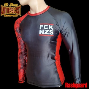 Pode incluir: Um rashguard de manga comprida em cinza e vermelho, com o texto "FCK NZS" em branco no peito. A manga esquerda tem um padrão vermelho e preto. A parte superior tem o texto "The Genuine Antifascist Fighting Club".