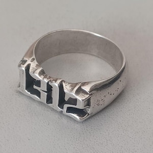 Puede incluir: Un anillo de plata con la palabra "ELF" grabada en una fuente gótica en negrita.