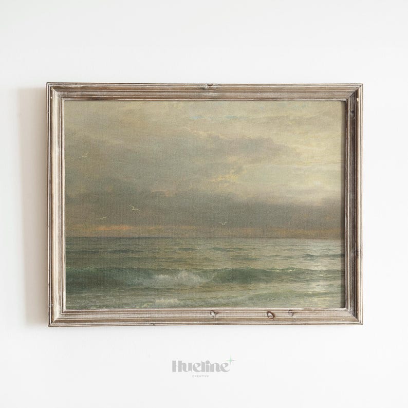May include: A framed vintage seascape painting. The artwork depicts a cloudy sky over a turbulent ocean with visible waves. The frame is a distressed, light-colored wood.