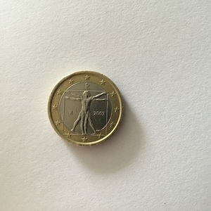 Puede incluir: Una moneda de un euro de color dorado con un centro plateado que representa al Hombre de Vitruvio, un famoso dibujo de Leonardo da Vinci. La moneda también tiene el año 2002 y la letra "R" inscrita en ella.