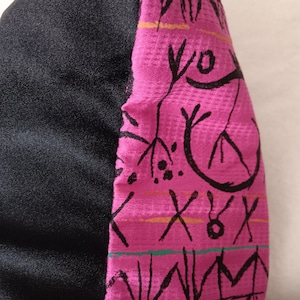 May include: A black and pink fabric with a geometric pattern. The pattern is made up of black lines and shapes on a pink background. The fabric is textured and has a slight sheen.