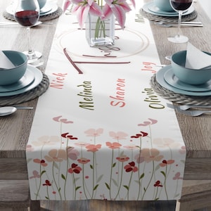 May include: White table runner with a floral design and the text "This is our" in a circle. The names Nick, Melinda, Sharon, Olivia, and Joy are written below the circle.
